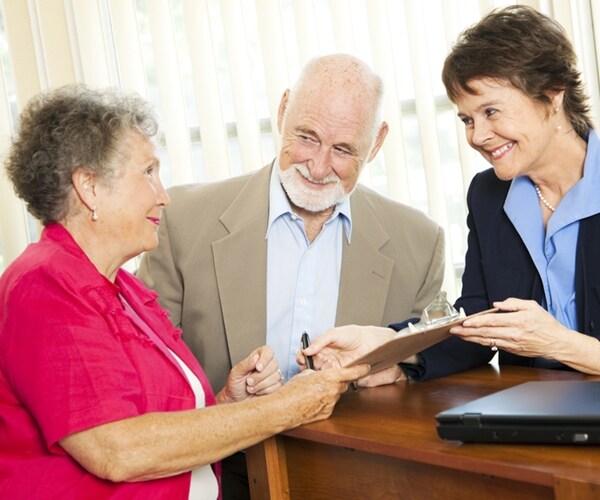 senior couple working with a broker or advisor, signing paperwork. 