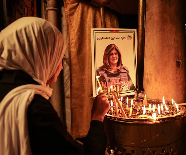 A woman lights a candle in front of a poster depicting veteran Al-Jazeera journalist Shireen Abu Akleh.