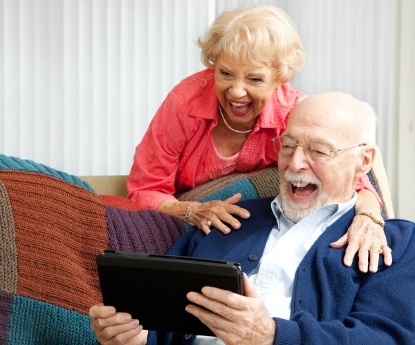 older man and woman laughing at something on a tablet