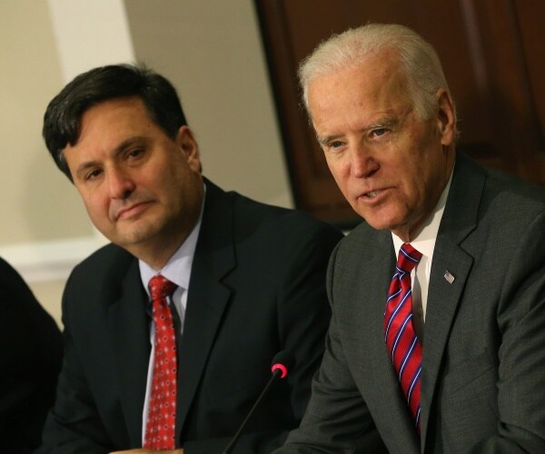 biden in a suit and striped tie sitting next to klain in a red tie