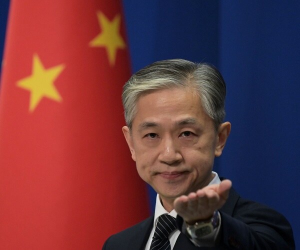 wang wenbin stands with arm outstretched in front of chinese flag