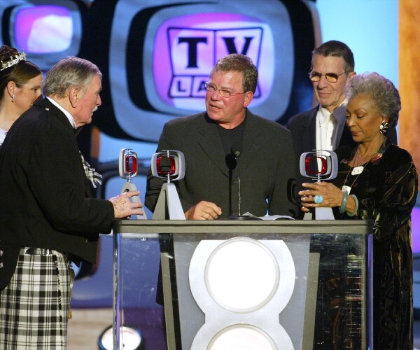 the actors standing behind a podium holding awards