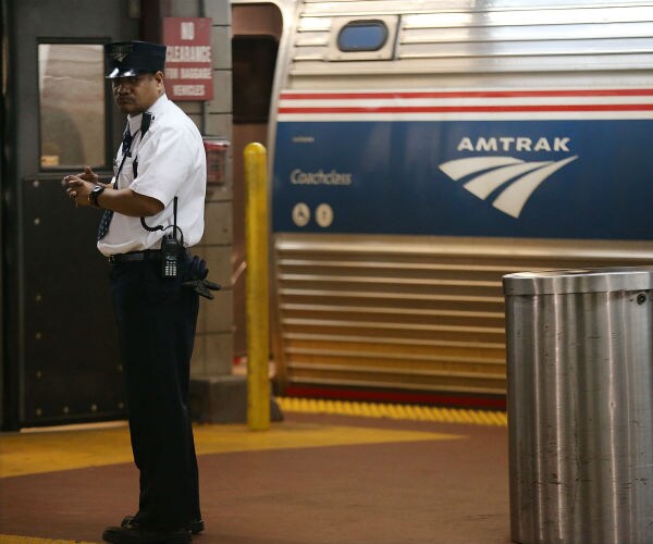 a train conductor, in uniform, stands next to an Amtrak train at New York's Pennsylvania Station