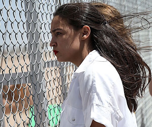 alexandria ocasio-cortez's black hair blows in the breeze as she peers through a chain-linked fence on the border