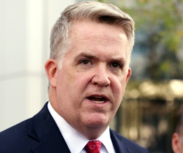 huber speaking outside wearing a navy blue suit and red tie