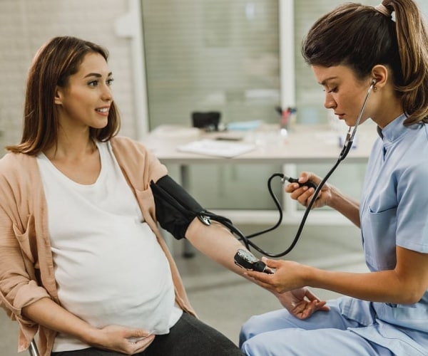 pregnant woman getting her blood pressure taken in doctor's office