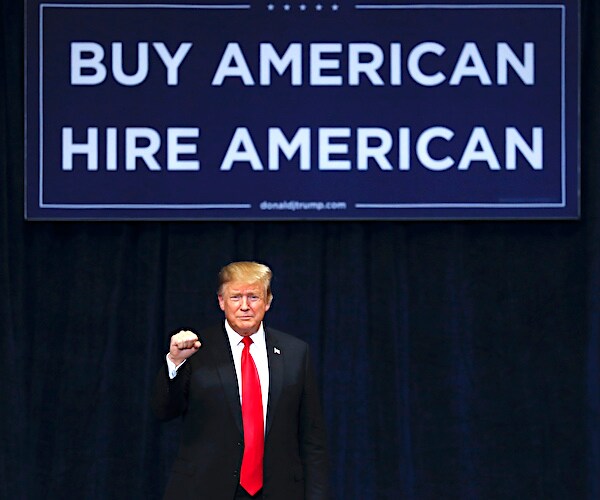 president donald trump pumps his right fist under a large sign that reads buy american, hire american