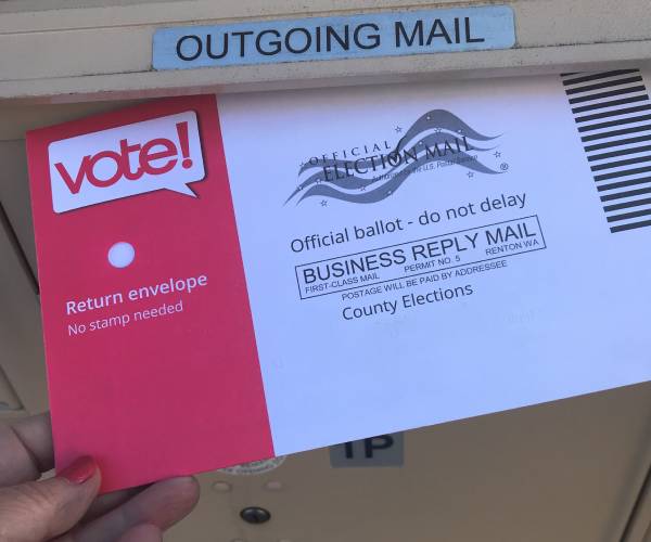 a person putting a mail in ballot in a mailbox