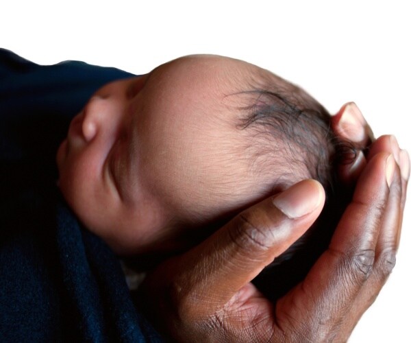 a black father's hand holding a black newborn baby