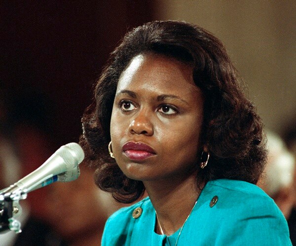 anita hill sits at a table listening to senators speak and ask questions during testimony
