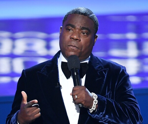 morgan in a velvet suit and black bowtie speaking into a mic