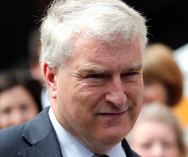 a briton man stands outside on a bright, sunny day, squinting in the sunlight