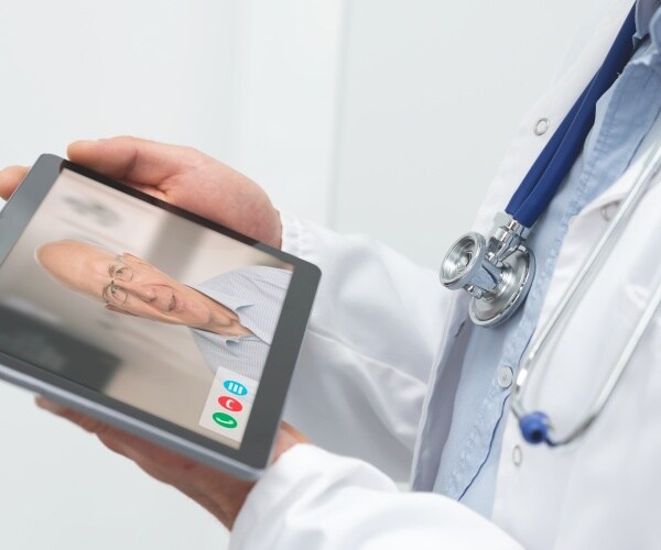physician holding a tablet with an older man on screen during a telemedicine visit