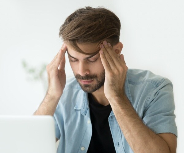 man feeling stressed at computer, holding his temples