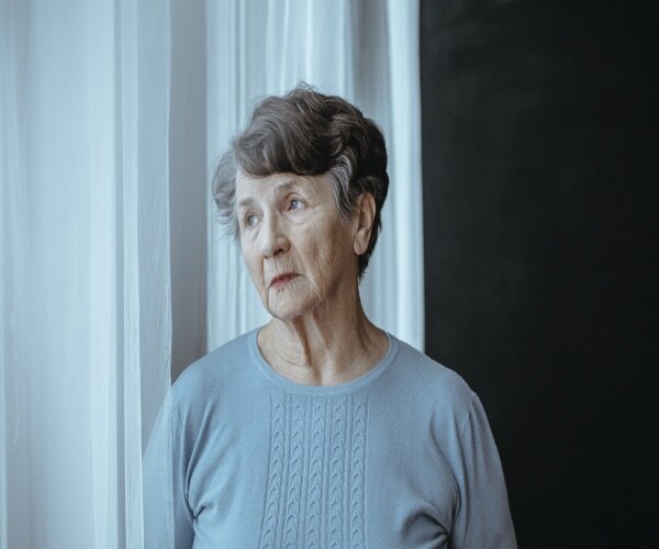 woman with alzheimer's looking out window with worried expression