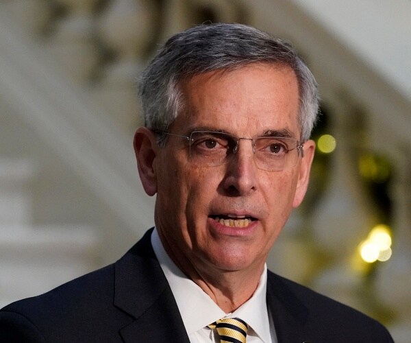 brad raffensperger stands behind podium