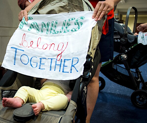 a migrant protester covers a baby in a stroller with a protest banner
