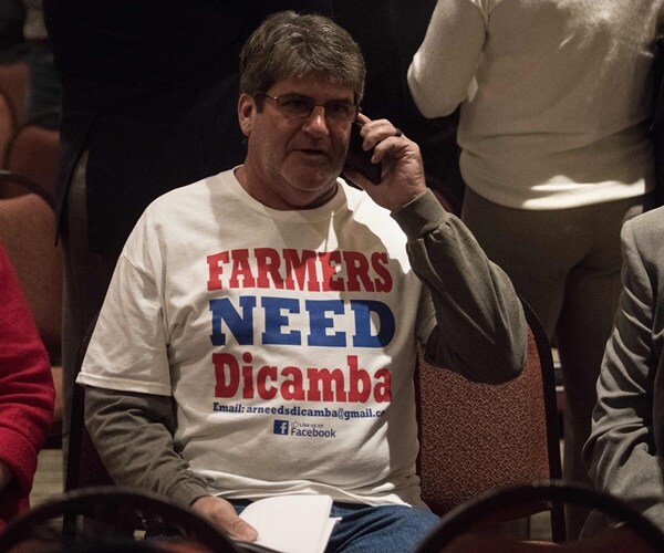a farmer sits at a hearing wearing a t-shirt in support of dicamba, an herbicide