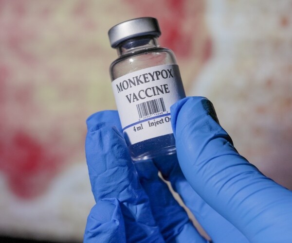 closeup of hand with surgical glove holding vial labeled 'monkeypox vaccine' 
