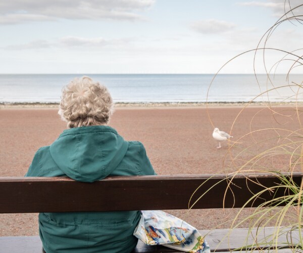 an elderly woman sitting on a bench at the beach by herself