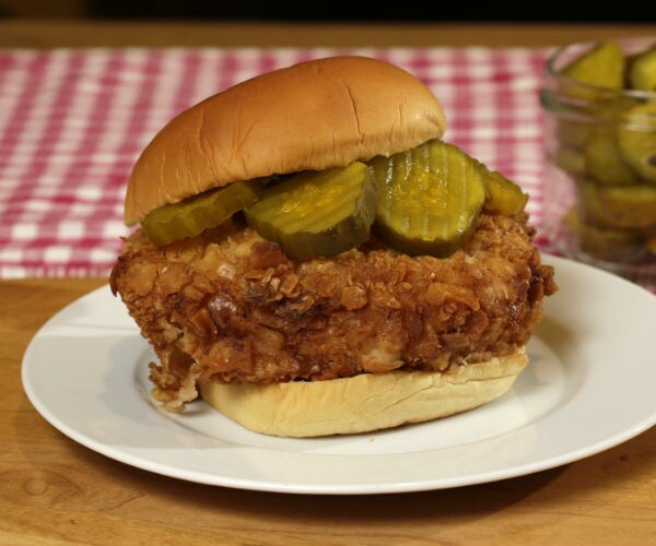 A fried chicken sandwich is shown with pickles on a bun.
