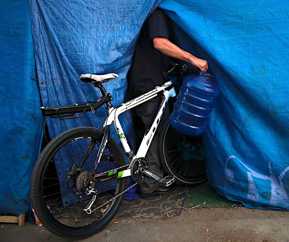 a bike is sticking out of the entrance of a tent as a man carries water in
