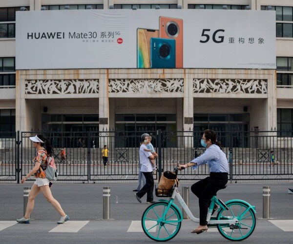 people walk and bike by a billboard advertising huawei 5g technology