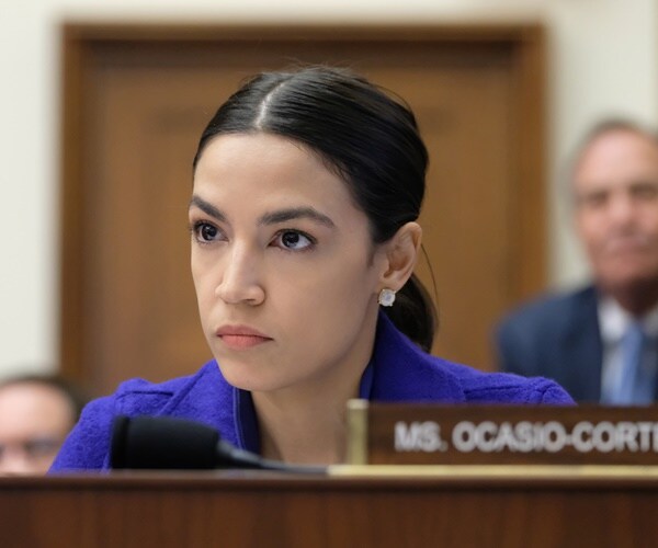 aoc seated in a hearing room listens to someone testify