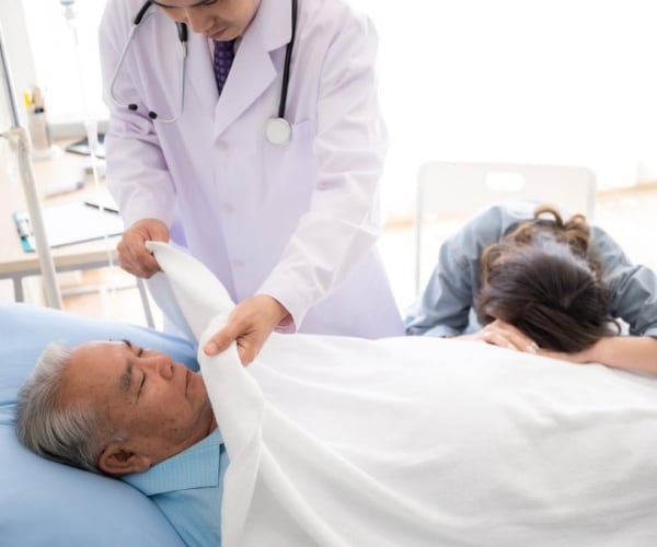 doctor putting sheet over dead patient in hospital as loved one cries