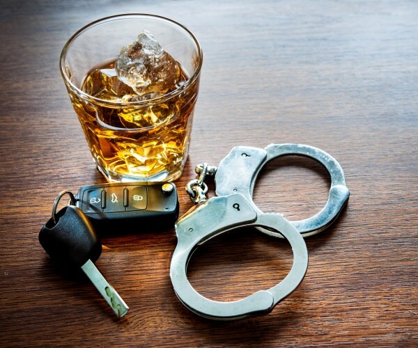 a glass of whiskey, car keys and handcuffs on a bar