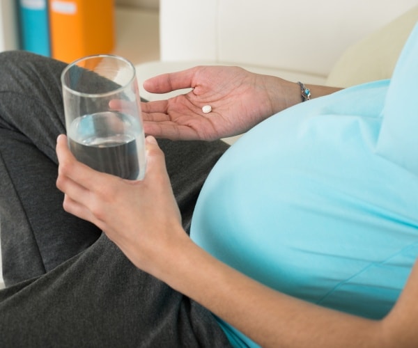 pregnant woman taking a pill with water