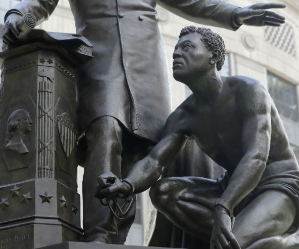 A detail of a statue that depicts a freed slave kneeling at Abraham Lincoln's feet rests on a pedestal