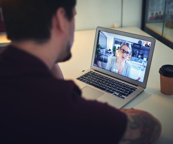 man at computer having a telehealth therapy session with female therapist on the screen