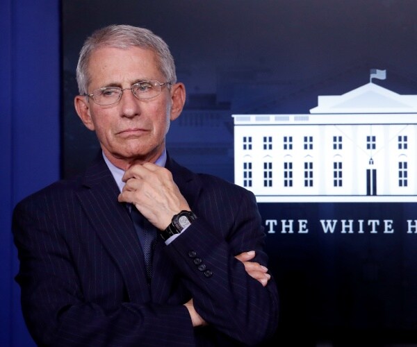 fauci in a suit and light blue shirt adjusting his collar