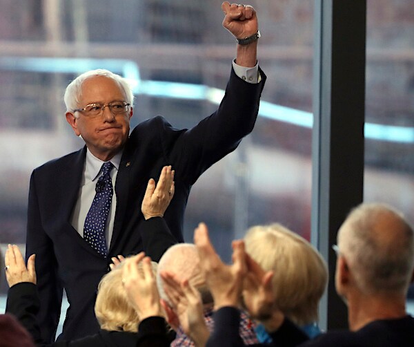 bernie sanders raises his left fist high in the air during a town hall