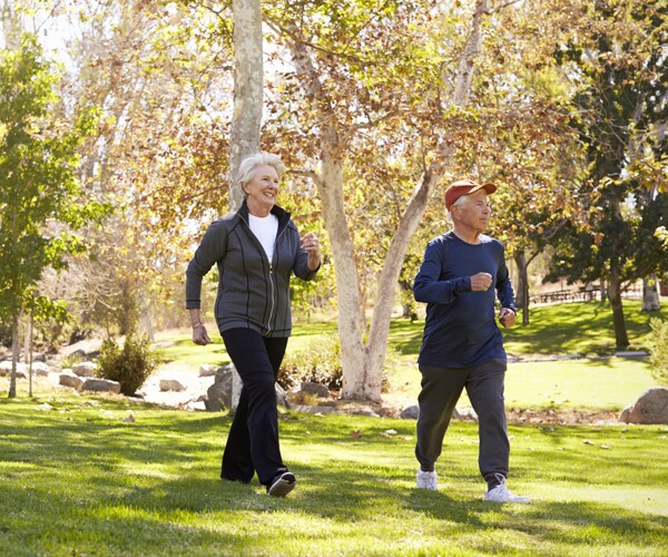 two senior citizens walking through a park on the grass
