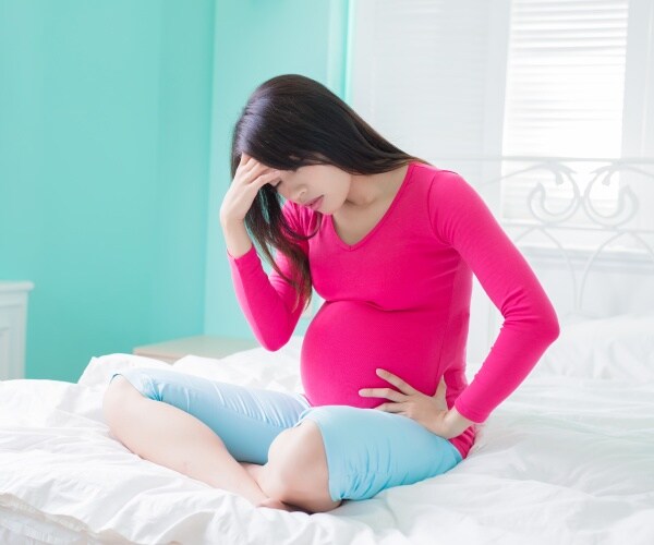 pregnant woman sitting on bed looking sad