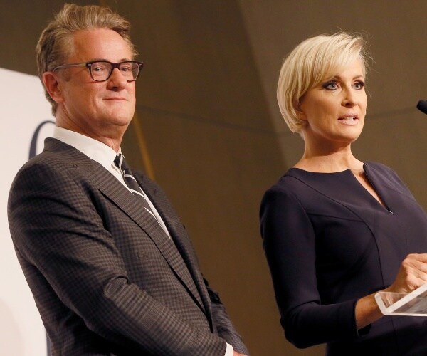 mika brzezinksi in a black dress speaking at a podium and joe scarborough in a gray suit standing and smiling