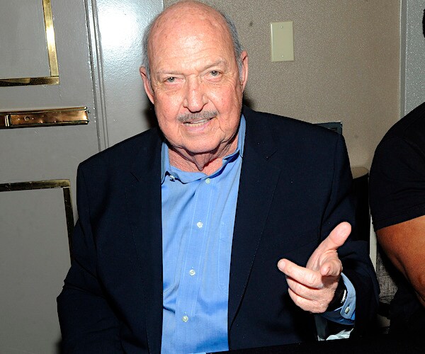 gene okerlund points his left index finger toward the camera while photographed by media at a hotel