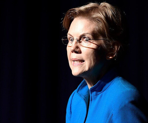 elizabeth warren stands and speaks on a dark stage