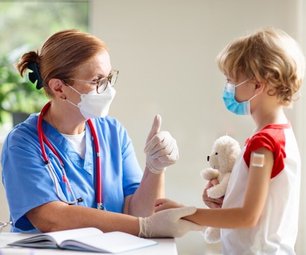 young child holding a stuffed animal after getting covid vaccine from healthcare worker, both giving thumbs up