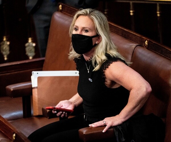 greene in a sleeveless black dress and black face mask holding her phone