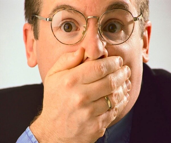 man holds hand in front of mouth with worried look