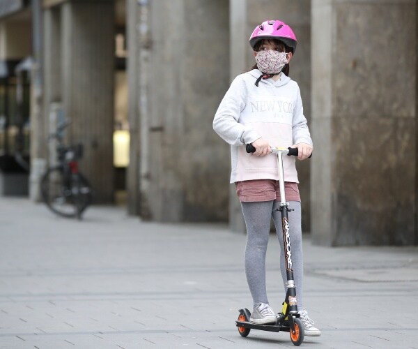 little girl riding a scooter wearing a face mask bike helmet gray leggings and a hoodie