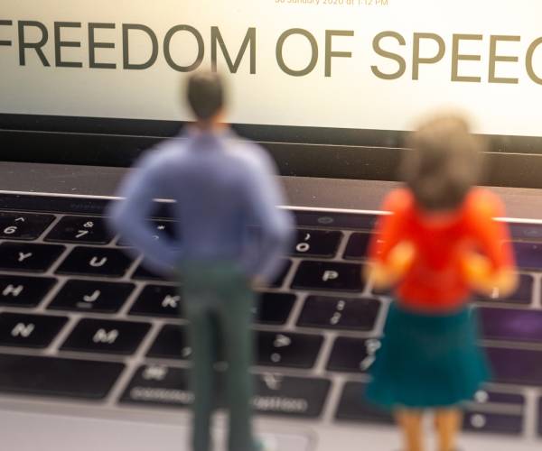 miniature figures of man and woman looking at laptop screen reading freedom of speech