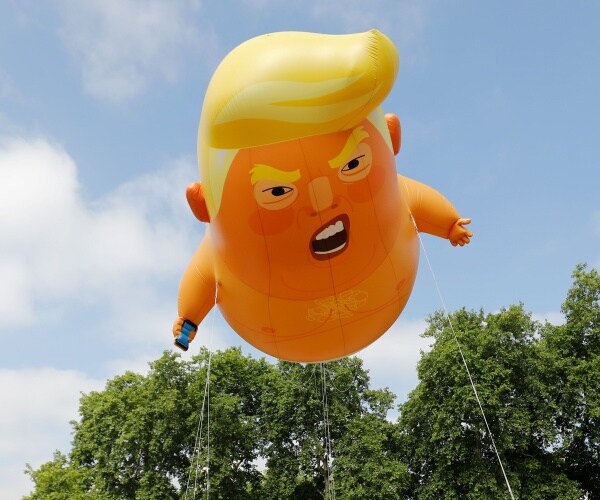 trump baby blimp is shown in the sky with trees nearby