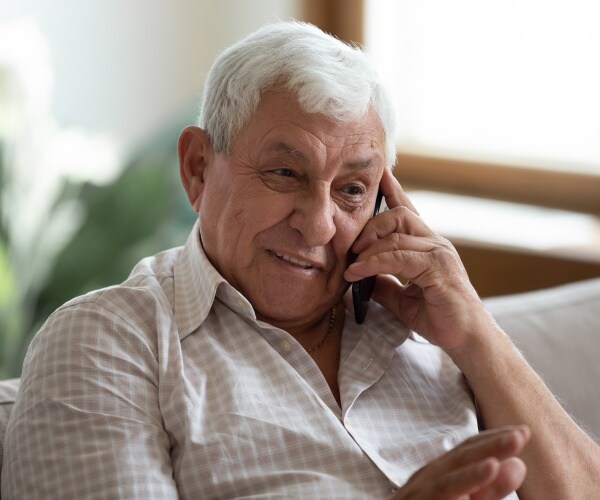 older man sitting on couch, smiling while talking on phone
