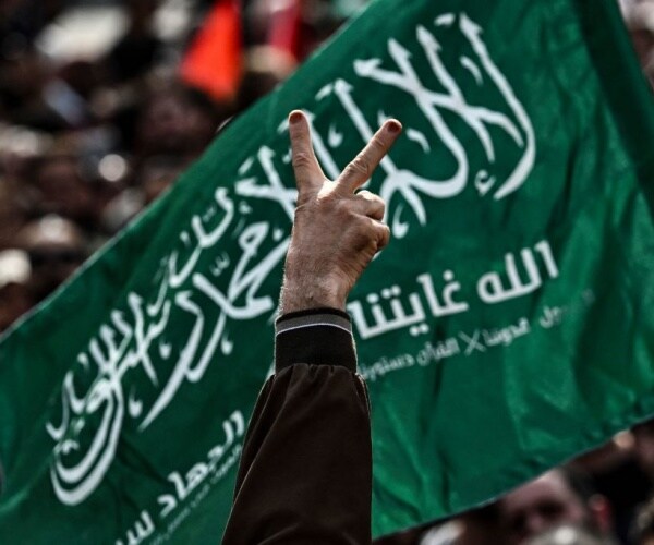 man flashes the victory sign against the flag of the hamas movement 