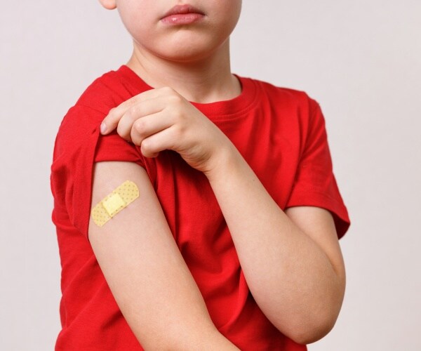 young boy shows arm with band-aid on it