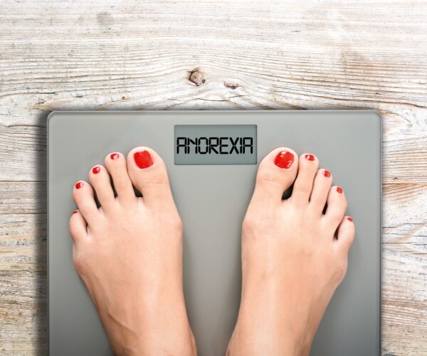 woman with red nail polish stands on a weight scale that says anorexia